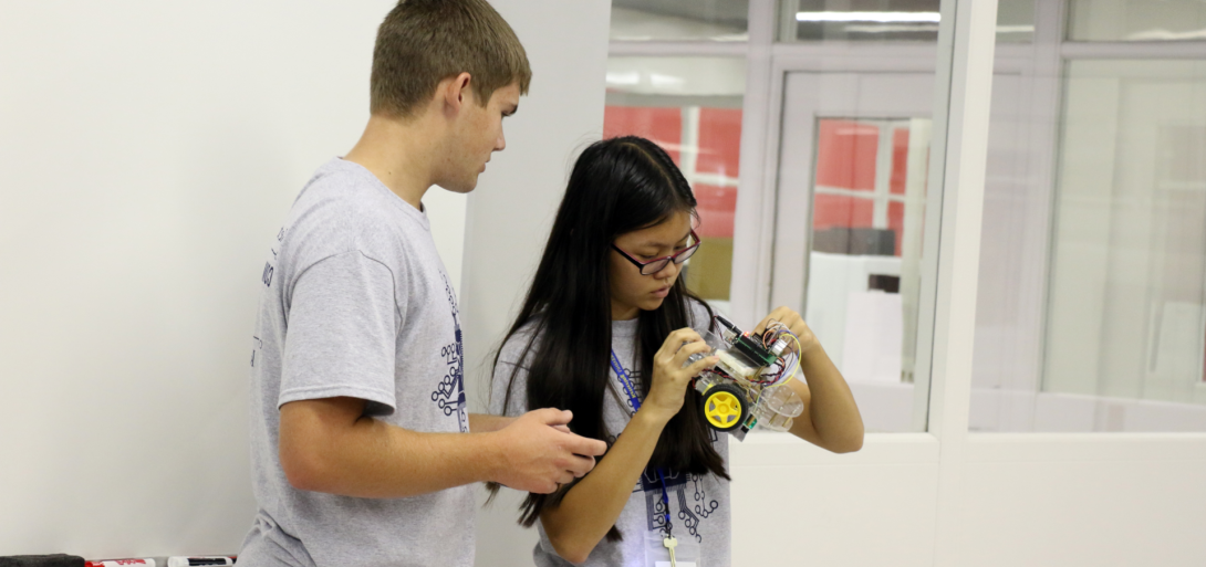 "Two students deeply engaged in hands-on robotics work, carefully examining and adjusting components of a small wheeled robot as part of a collaborative STEM project in a modern classroom setting."