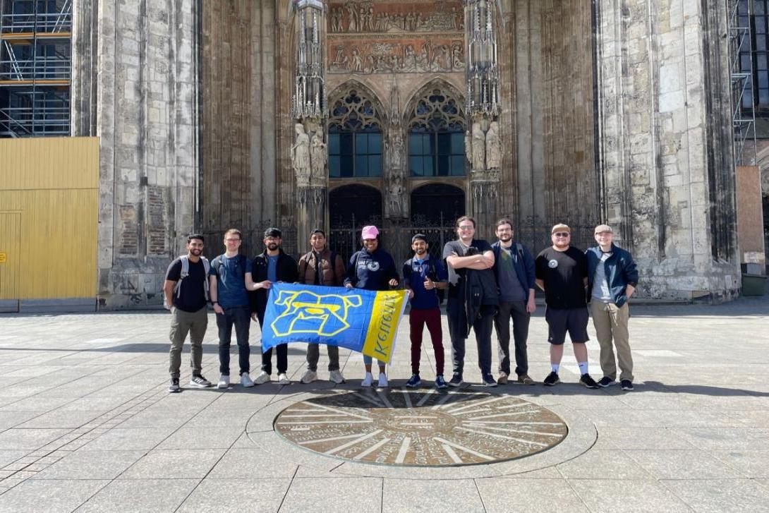 Kettering students stand in front of a historic church in Germany and hold up a Kettering banner